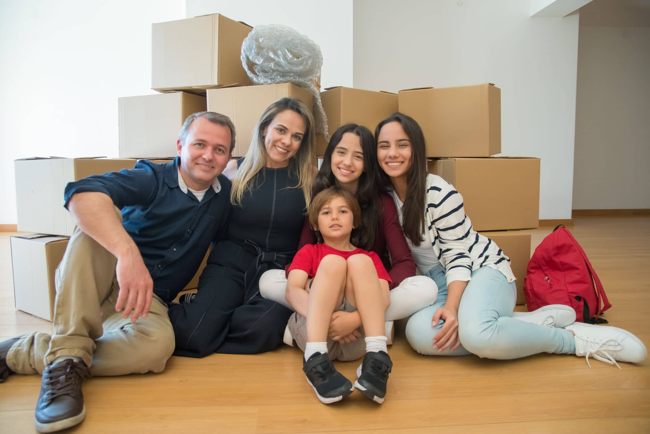Família sorrindo sentada no chão da casa nova, entre caixas de mudança
